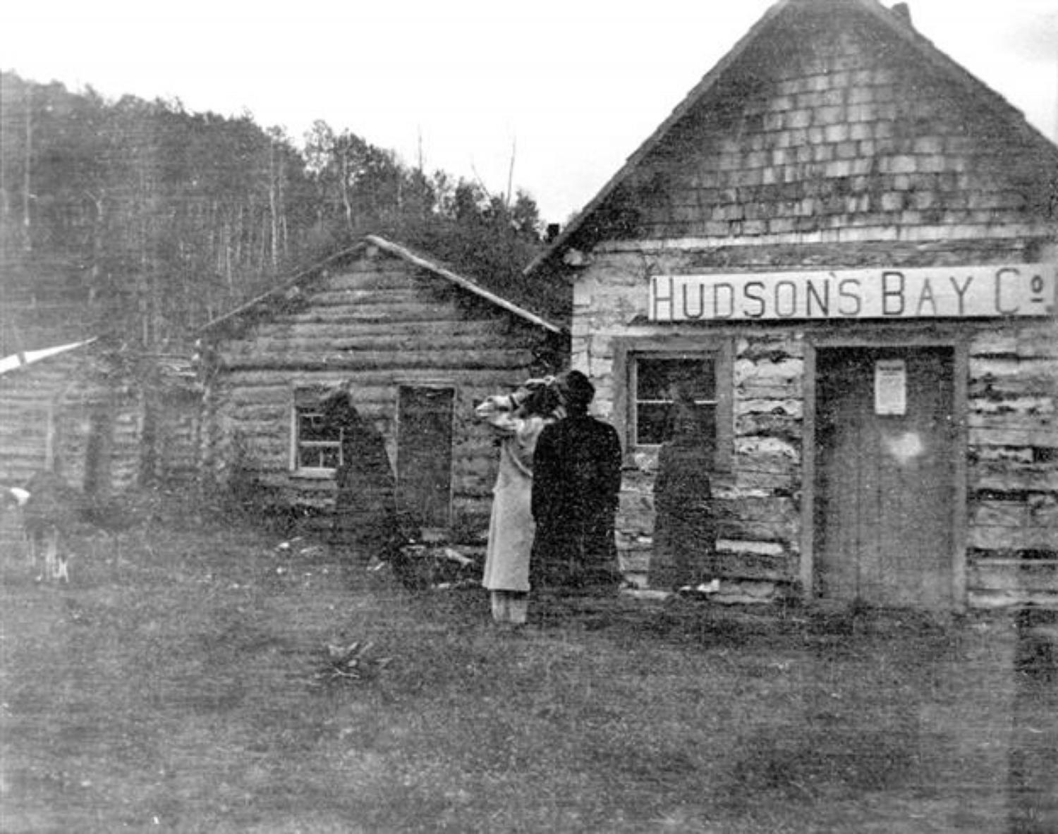 View of the exterior of a Hudson's Bay Company Tranding Post at Athabasca Landing, showing two unidentified people outside door.