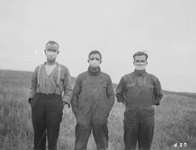 Three men wearing face masks in a field