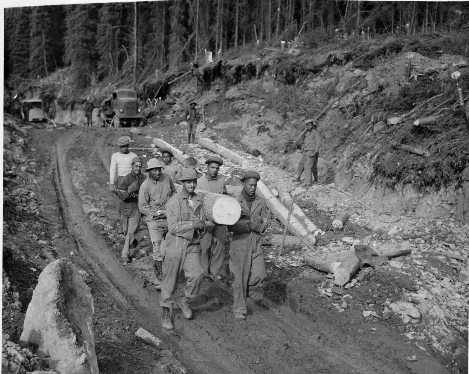African-American men hauling log down cleared, muddy road during construction of the ALCAN. 