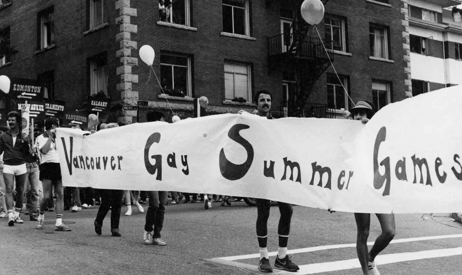 People crossing a street bearing a banner reading "Vancouver Gay Summer Games"