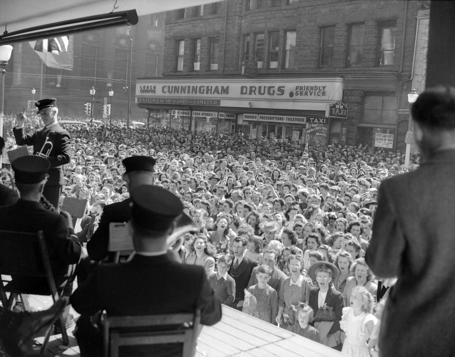 Black and white photo of large street crowd celebrating end of European theatre in WWII.