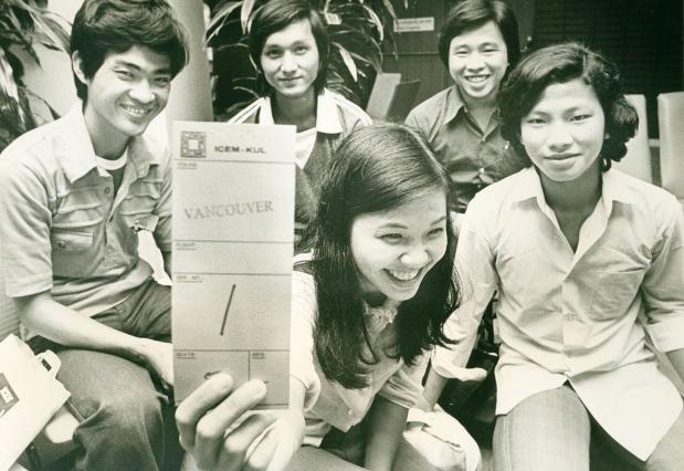 Young, smiling Vietnamese refugees holding up a sign with 'Vancouver' written on it.