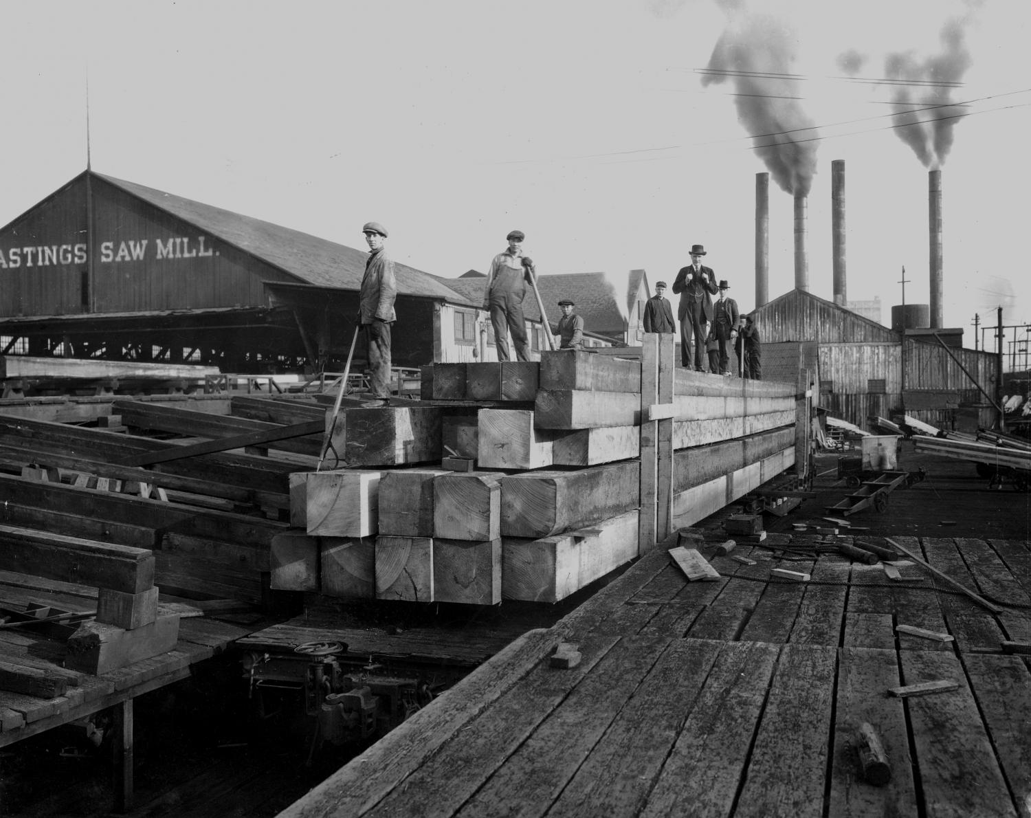 Large timbers being loaded onto flat cars at Hastings Sawmill, Chinese men working, Strathcona, Vancouver, B.C.