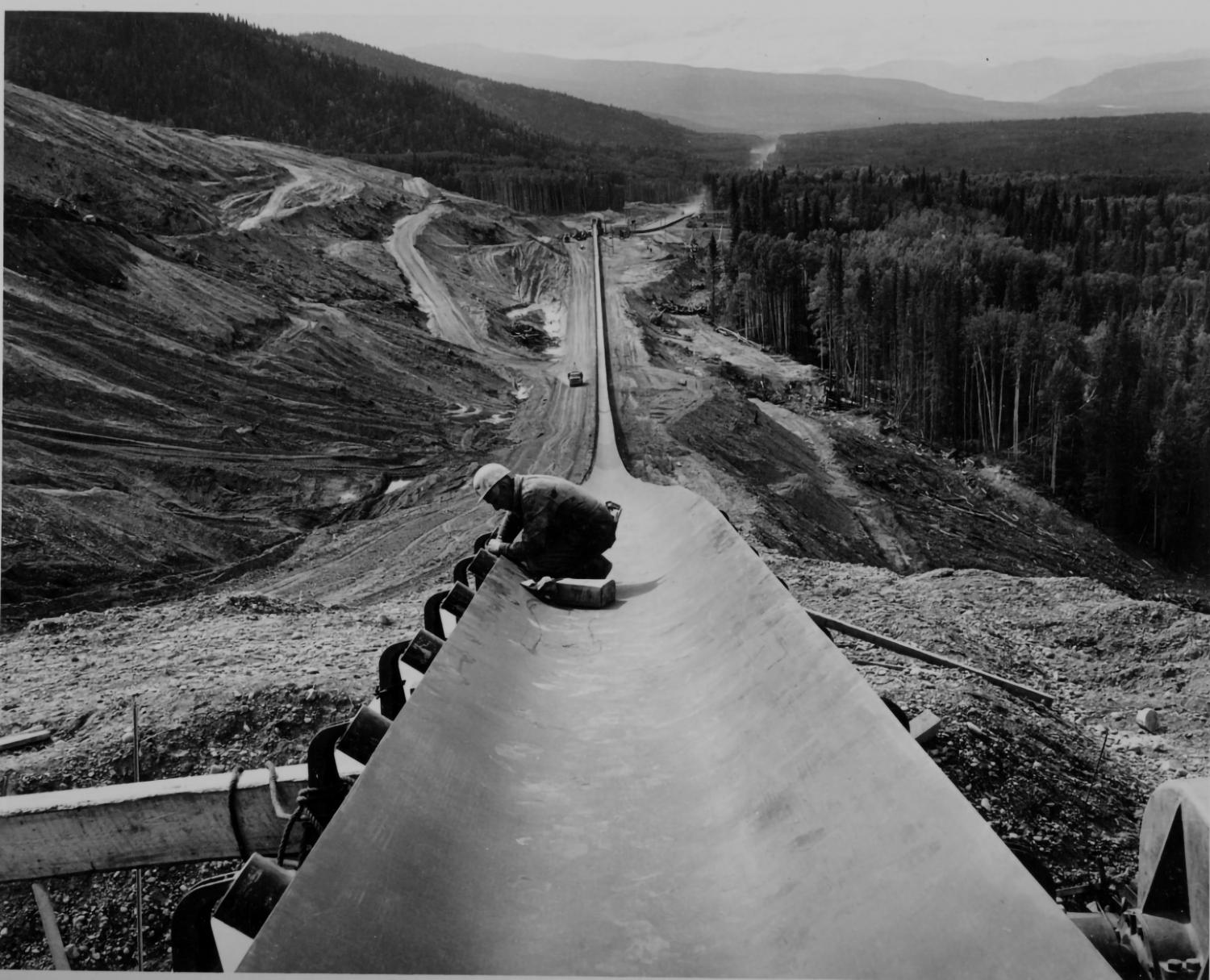 A construction worker working on a long trough during the building of the Portage Mountain dam.