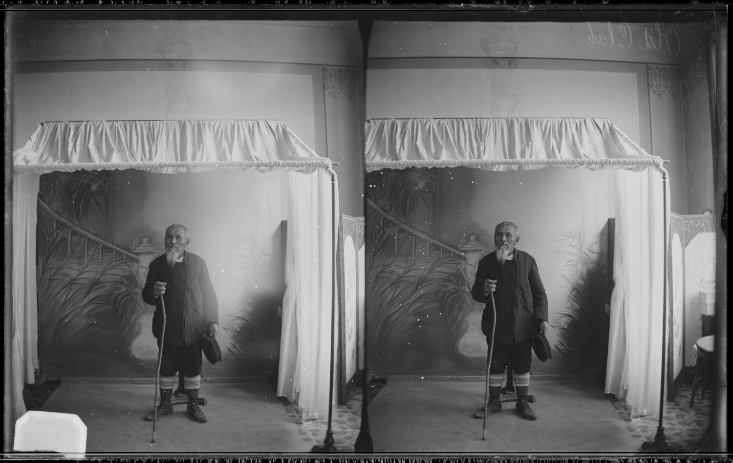 Portrait (full-length) of an unidentified Indigenous individual, likely Tsimshian Chief Arthur Wellington Clah, standing taken at a photographic studio attributed to Mrs. R. Maynards Photographic Gallery.