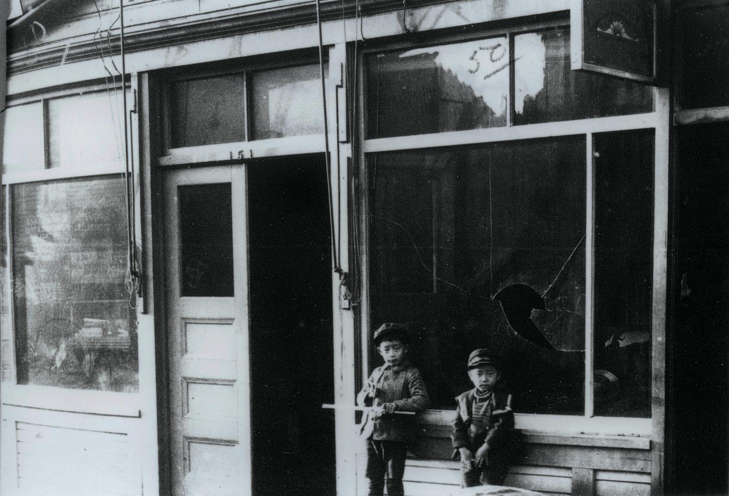 Photo of two young children outside a business that was damaged in 1907 anti-Asian riot.