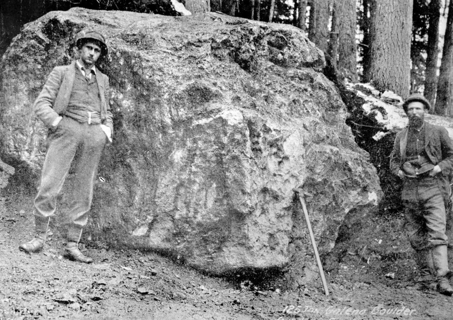 Two men stand with a giant boulder